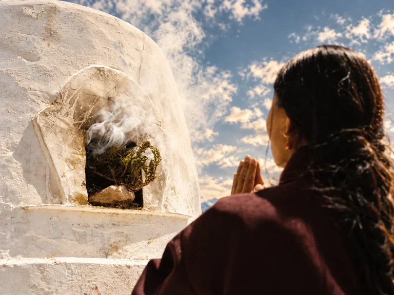 A person making an outdoor juniper incense offering beside a whitewashed incense burner