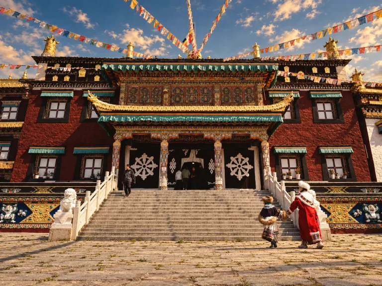 Visitors approaching a Tibetan-style monastery in warm afternoon light